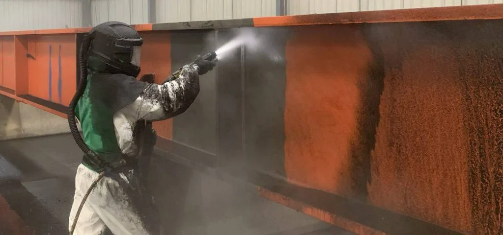 AAH operator abrasive blasting a structural steel beam