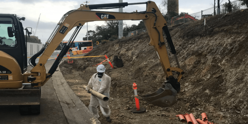CAT construction vehicle digging a trench with man in protective gear